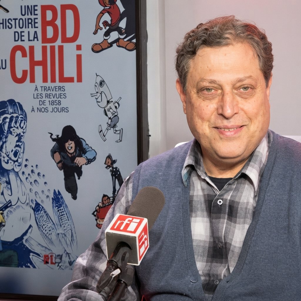 Moisés Hassón durante una entrevista, junto a un afiche de cómic
