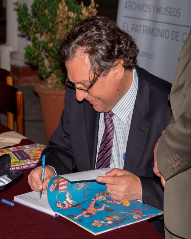 Moisés Hassón, con gafas y traje, firmando un libro de historietas